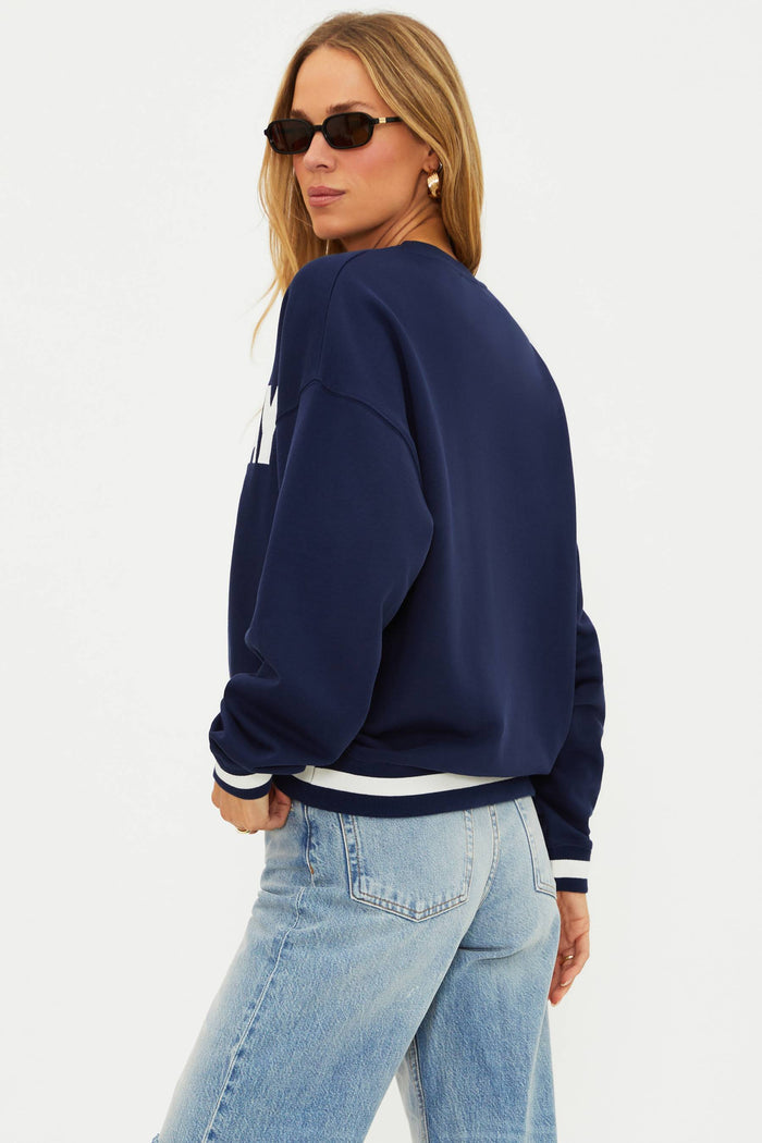Woman wearing a navy blue sweatshirt with white text and light blue jeans on a white background