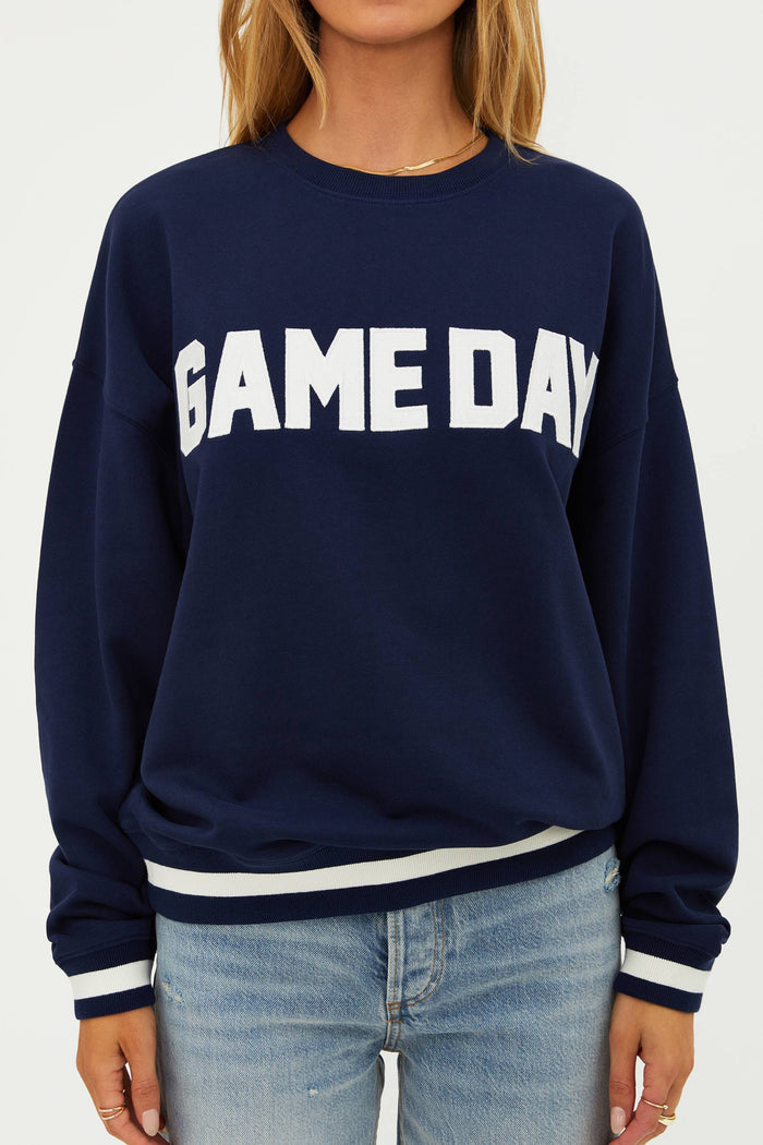 Navy sweatshirt with 'GAME DAY' text worn by a person on a white background
