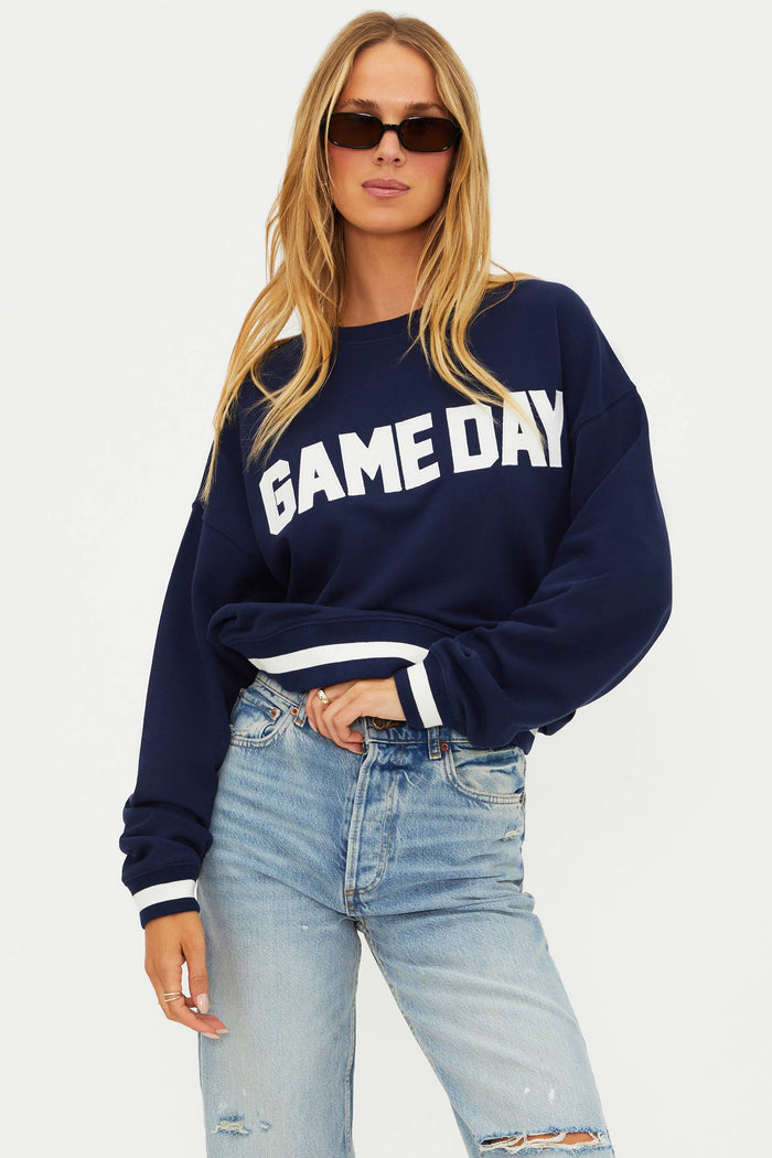Woman wearing a navy 'GAME DAY' sweatshirt and light blue jeans on a white background