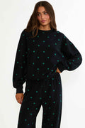 Woman wearing a black sweater and pants with green patterns on a white background