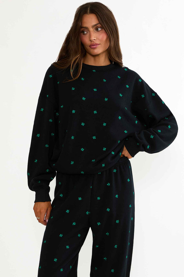 Woman wearing a black sweater and pants with green patterns on a white background