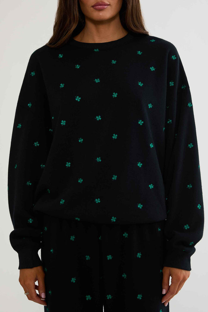 Black sweater with green pattern worn by a person on a white background