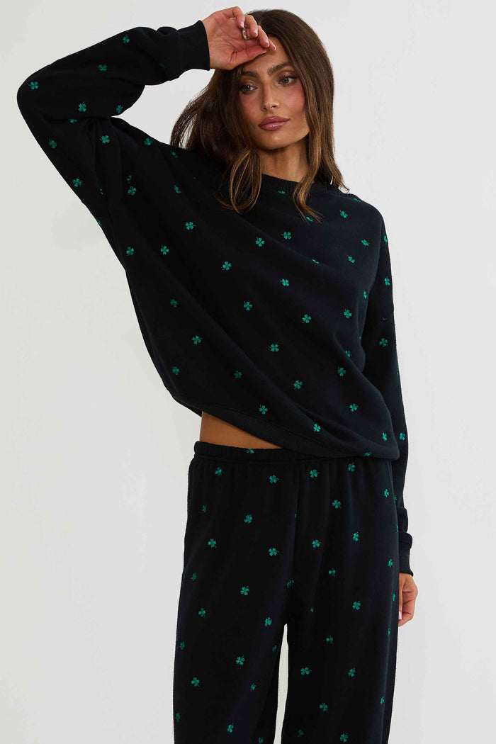 Woman wearing a black sweater and pants with green patterns on a white background