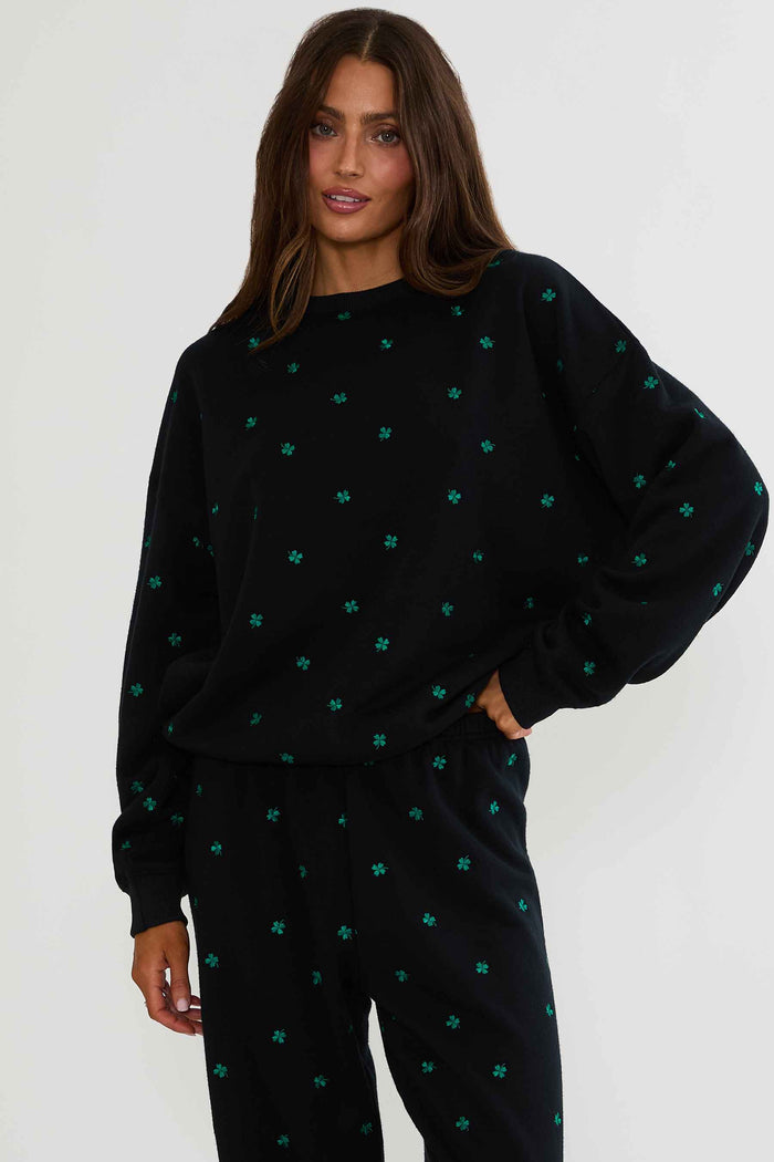 Woman wearing a black sweater with green patterns on a white background