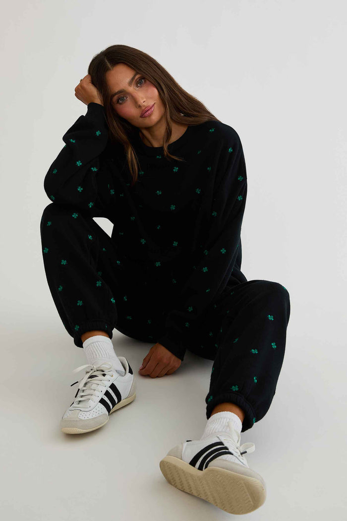 Person wearing a black outfit with green polka dots and white sneakers on a white background