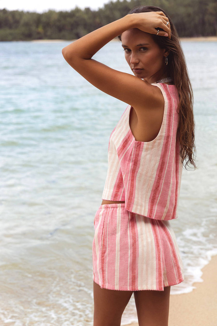 Woman in a pink and white striped outfit standing by a body of water.