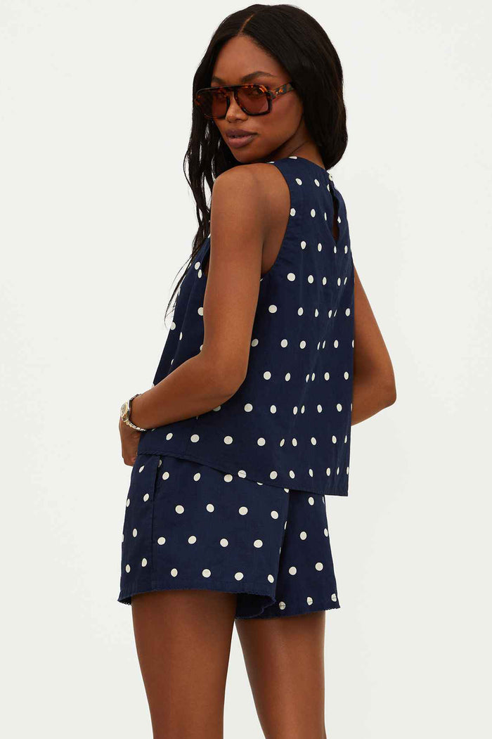 Model wearing a navy sleeveless top with white polka dots, paired with matching shorts, accessories include sunglasses and a watch.