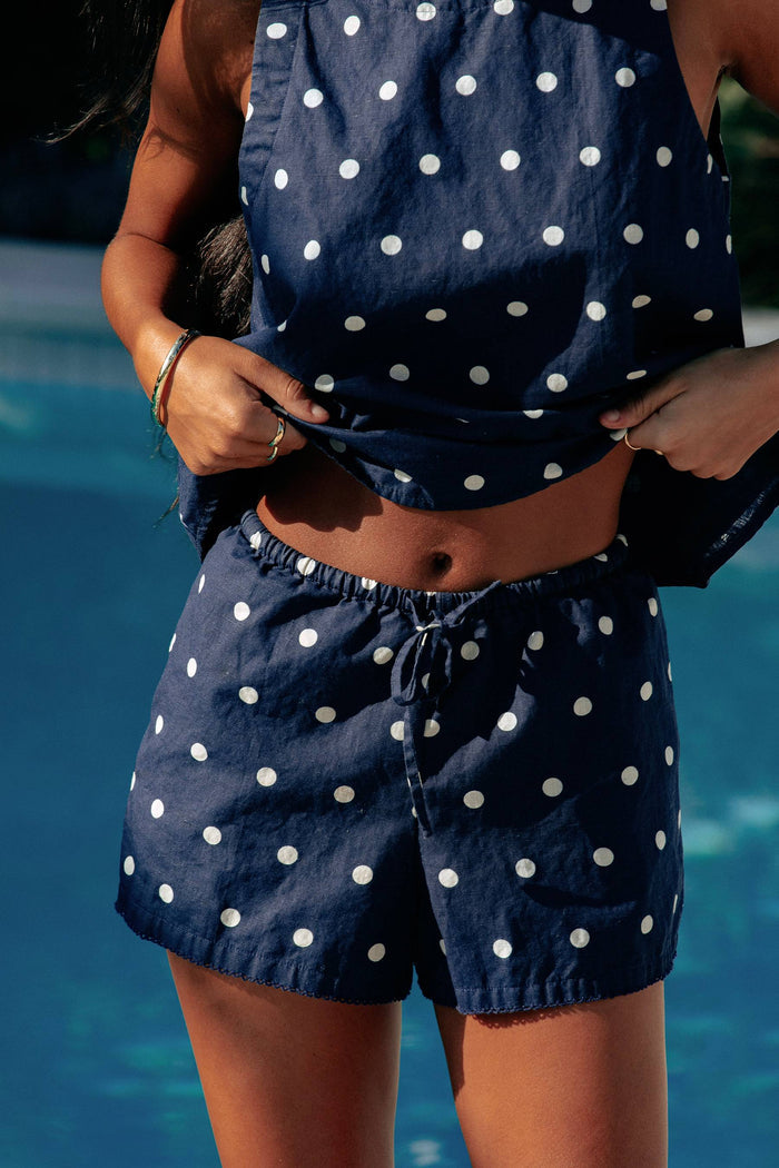Model wearing a navy sleeveless top with white polka dots, paired with matching shorts, accessories include sunglasses and a watch.