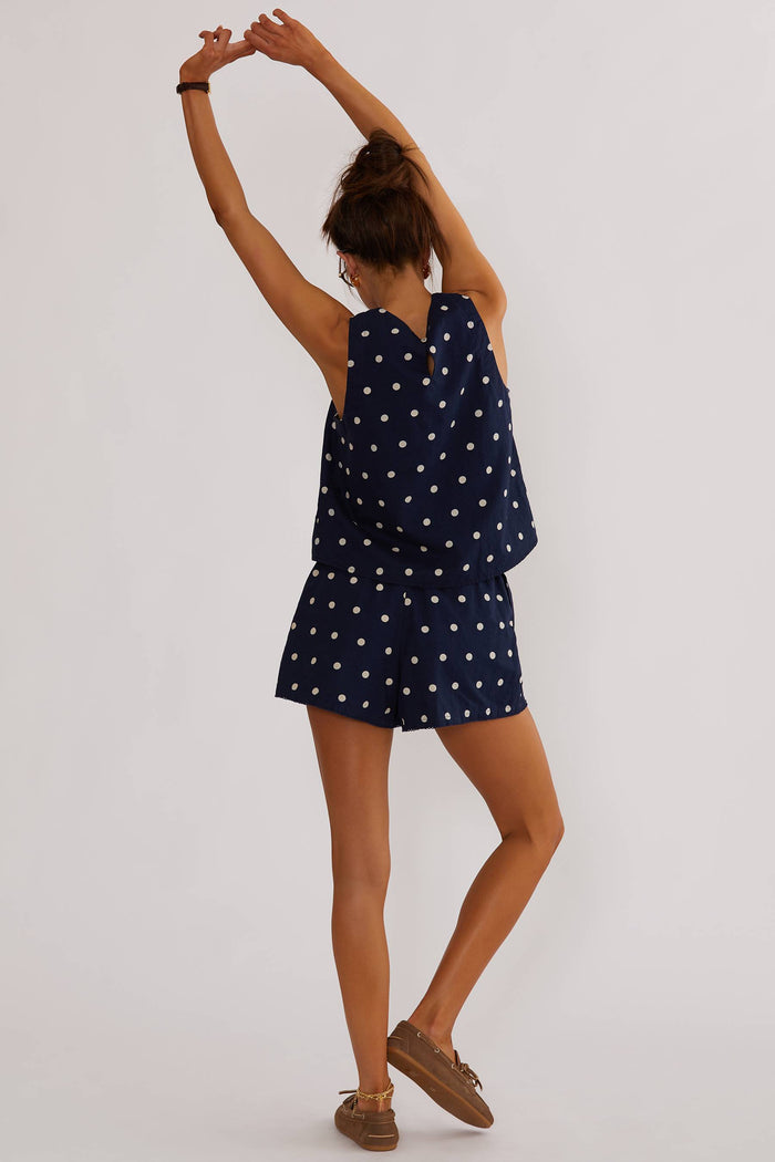 Model wearing a navy sleeveless top with white polka dots, paired with matching shorts, accessories include sunglasses and a watch.
