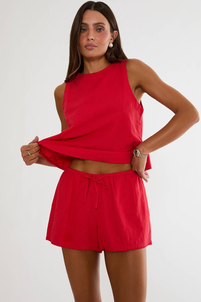 Woman wearing a red sleeveless top and shorts on a white background