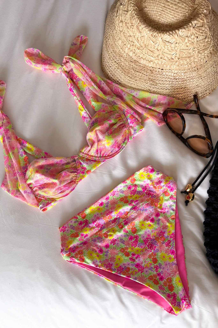 Floral bikini set with a straw hat and sunglasses on a white surface