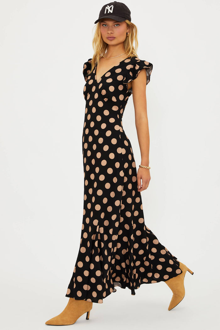 Woman wearing a black polka dot dress with beige dots on a white background