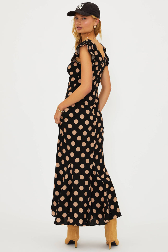 Woman wearing a black polka dot dress and a black cap on a white background