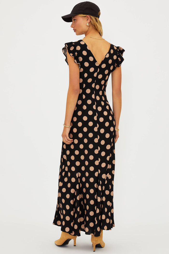Woman wearing a black dress with beige polka dots and a cap hat on a white background