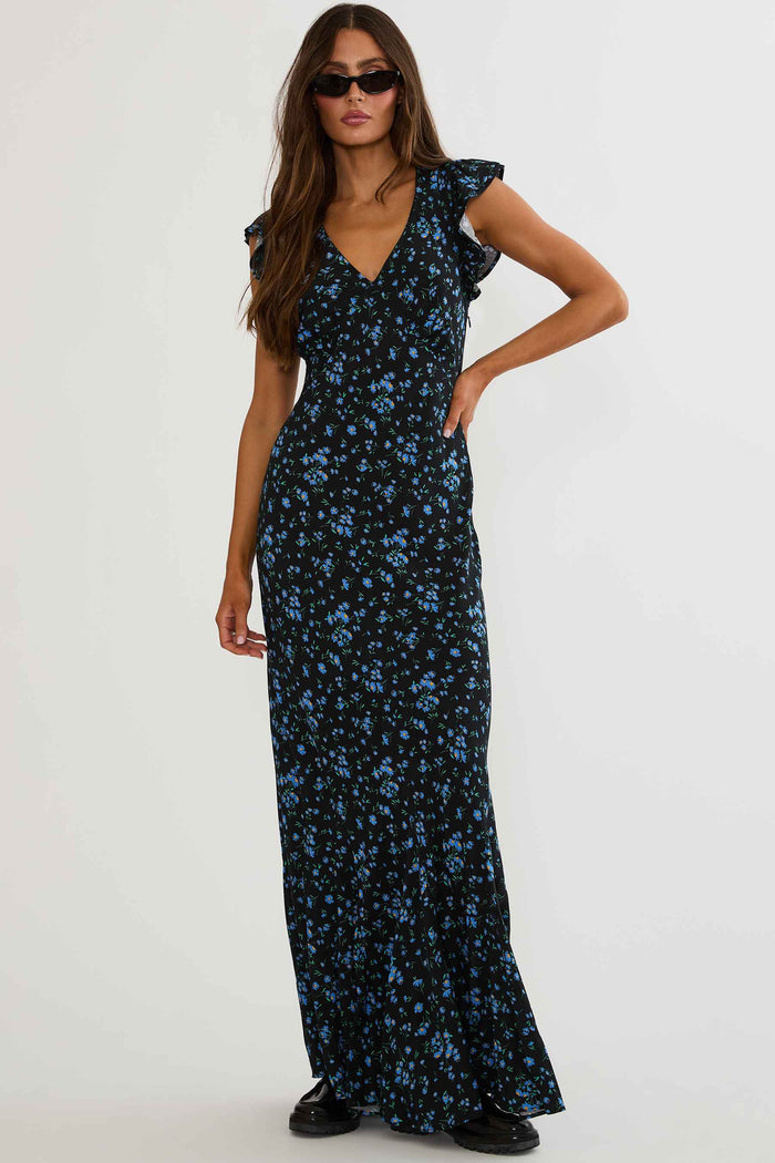 Woman wearing black maxi dress with blue florals on a white background.