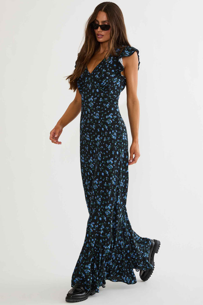 Woman wearing black maxi dress with blue florals on a white background.