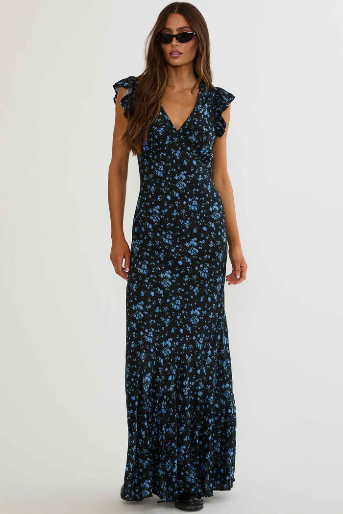 Woman wearing black maxi dress with blue florals on a white background.