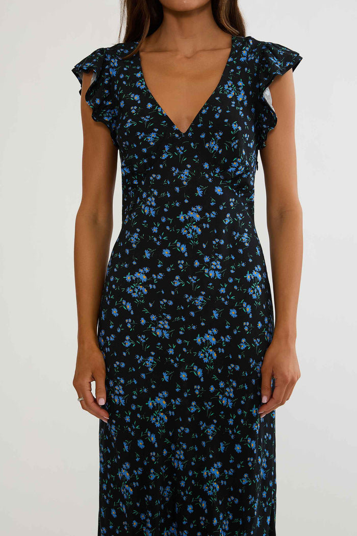Woman wearing black maxi dress with blue florals on a white background.
