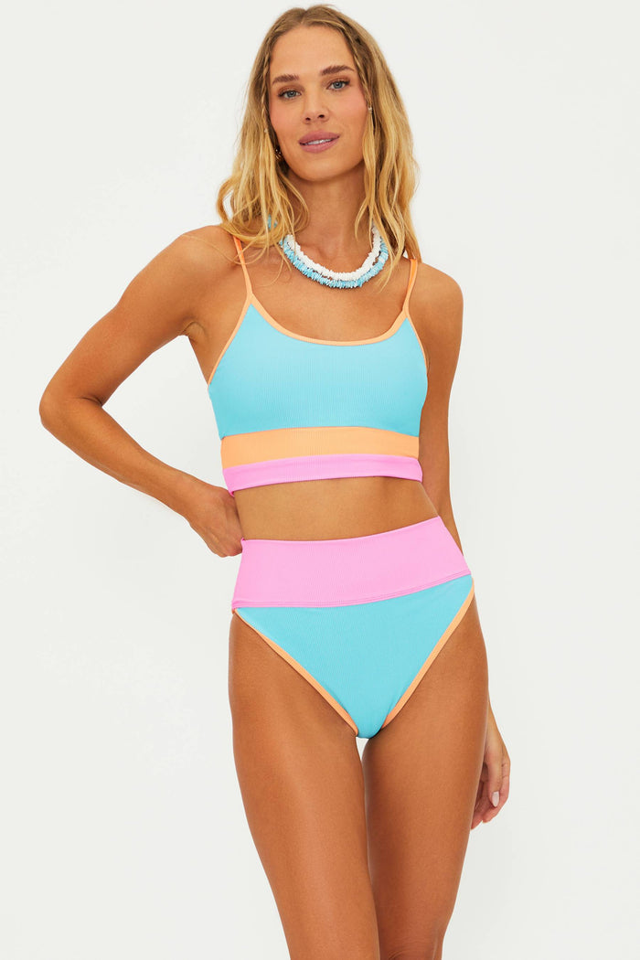 A model wearing a colorblock swim top in blue, pink, and orange with matching high-waisted bottoms.
