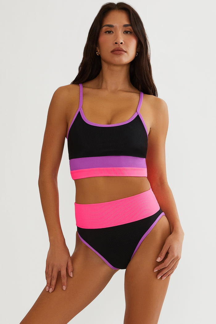 Woman wearing a colorful two-piece swimsuit with black, pink, and purple hues on a white background.