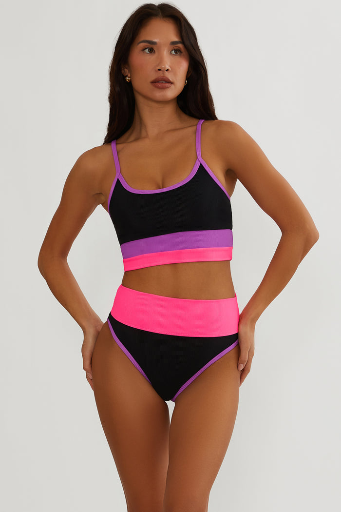 Woman wearing a colorful bikini set with black, pink, and purple straps on a white background