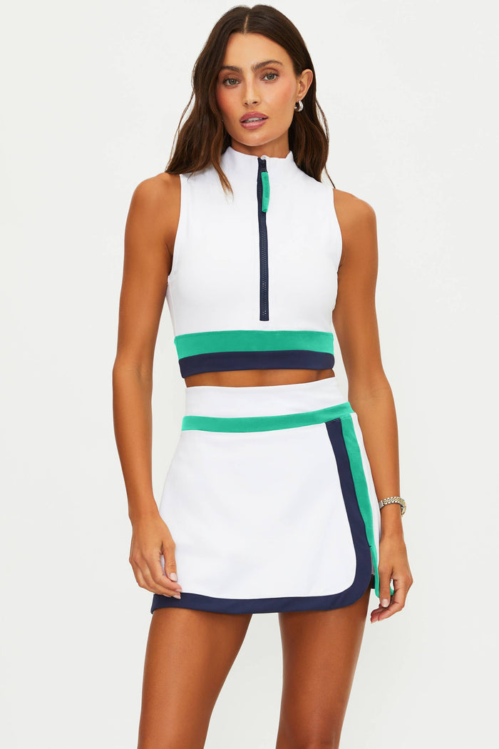 Woman wearing a white sleeveless top and skirt with green and navy accents on a white background