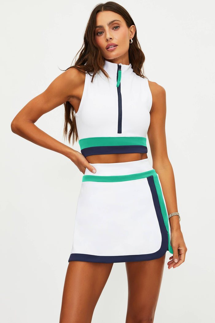Woman wearing a white sleeveless top and skirt with green and navy accents on a white background