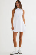 A woman modeling a sleeveless white dress with a small turquoise zipper at the neckline, paired with white socks and white sneakers, against a plain white studio background.
