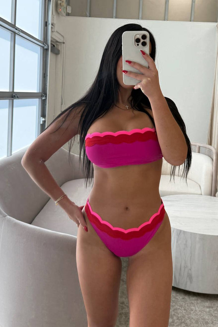 Person wearing a pink bikini taking a mirror selfie in a room with white walls and a window.