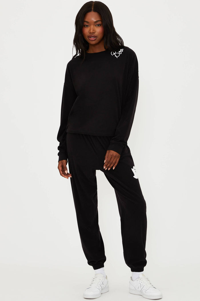 Person wearing a black tracksuit with white sneakers on a white background