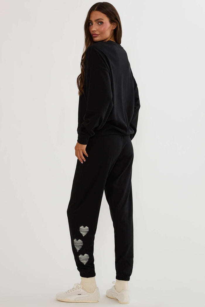 Black sweatpants with white hearts on the side worn by a woman on a plain white background.