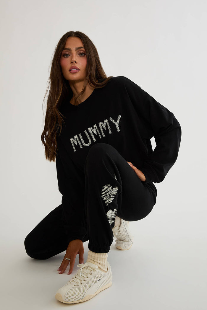 Black sweatpants with white hearts on the side worn by a woman on a plain white background.