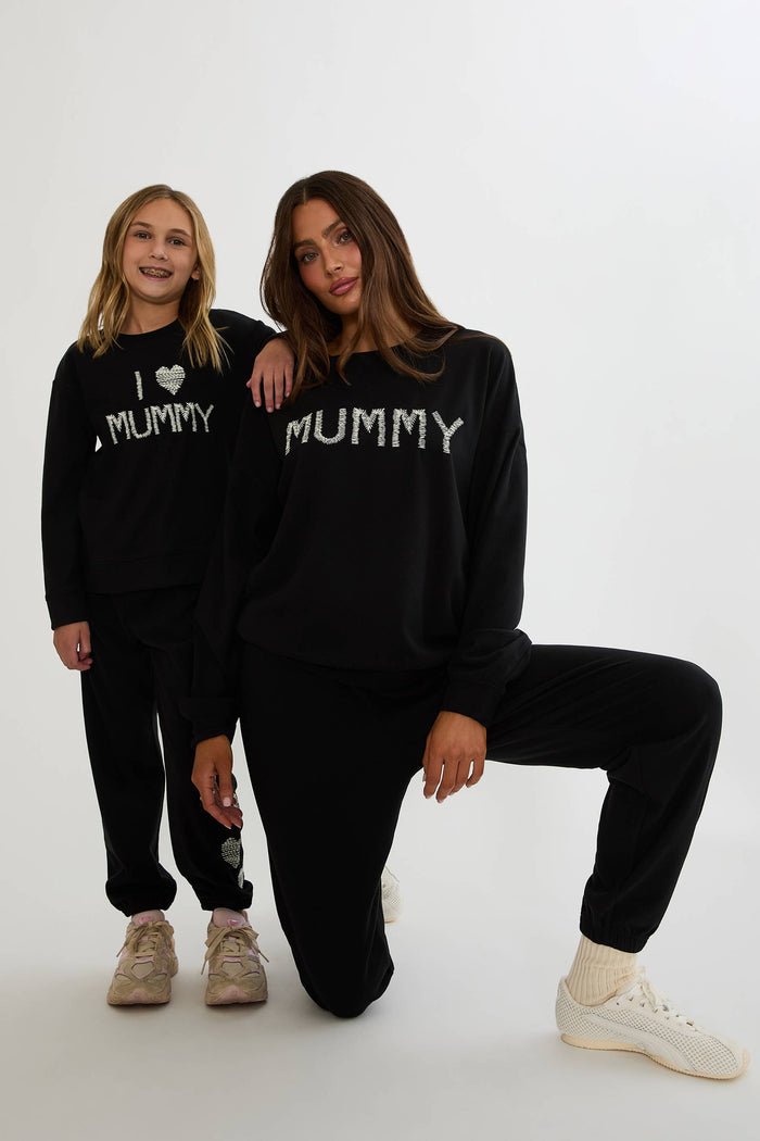 Black sweatpants with white hearts on the side worn by a woman on a plain white background.