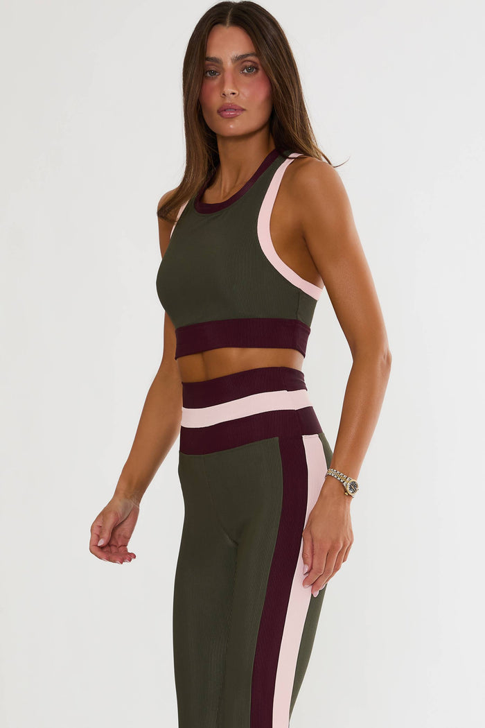 A woman modeling a matching color-blocked activewear set consisting of a cropped tank top and high-waisted leggings. The set features an olive green base with contrasting bands of deep burgundy and light pink.