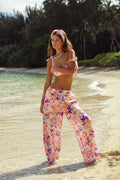 Woman in a pink floral outfit standing on a beach with greenery in the background