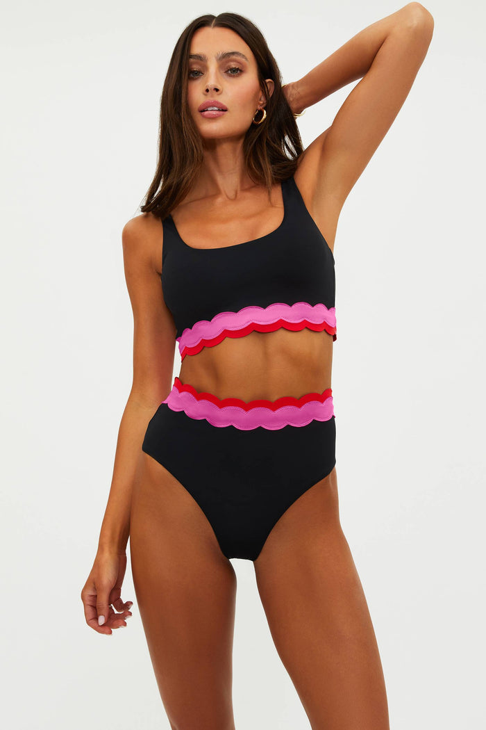 Woman wearing a black bikini with pink and red scalloped details on a white background