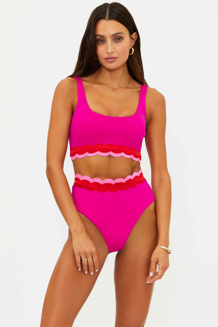 Woman wearing a bright pink swimsuit with scalloped details on a white background