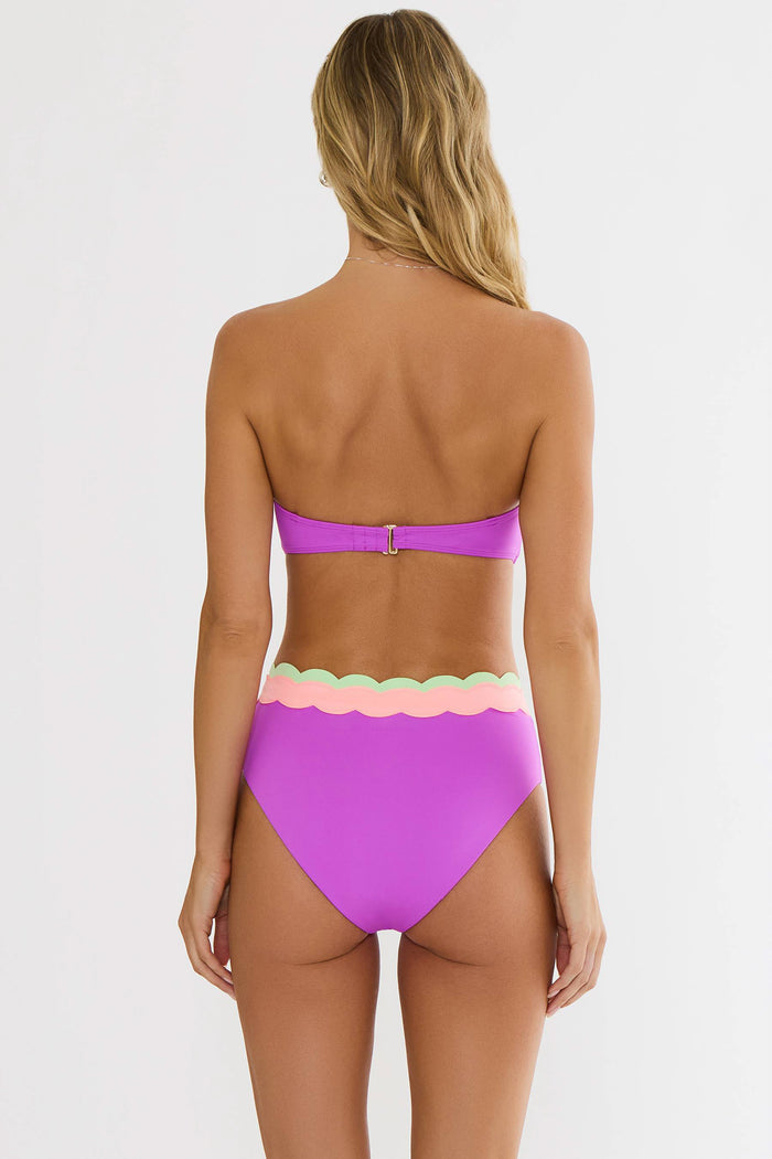 Woman wearing a pink bikini with scalloped edges on a white background
