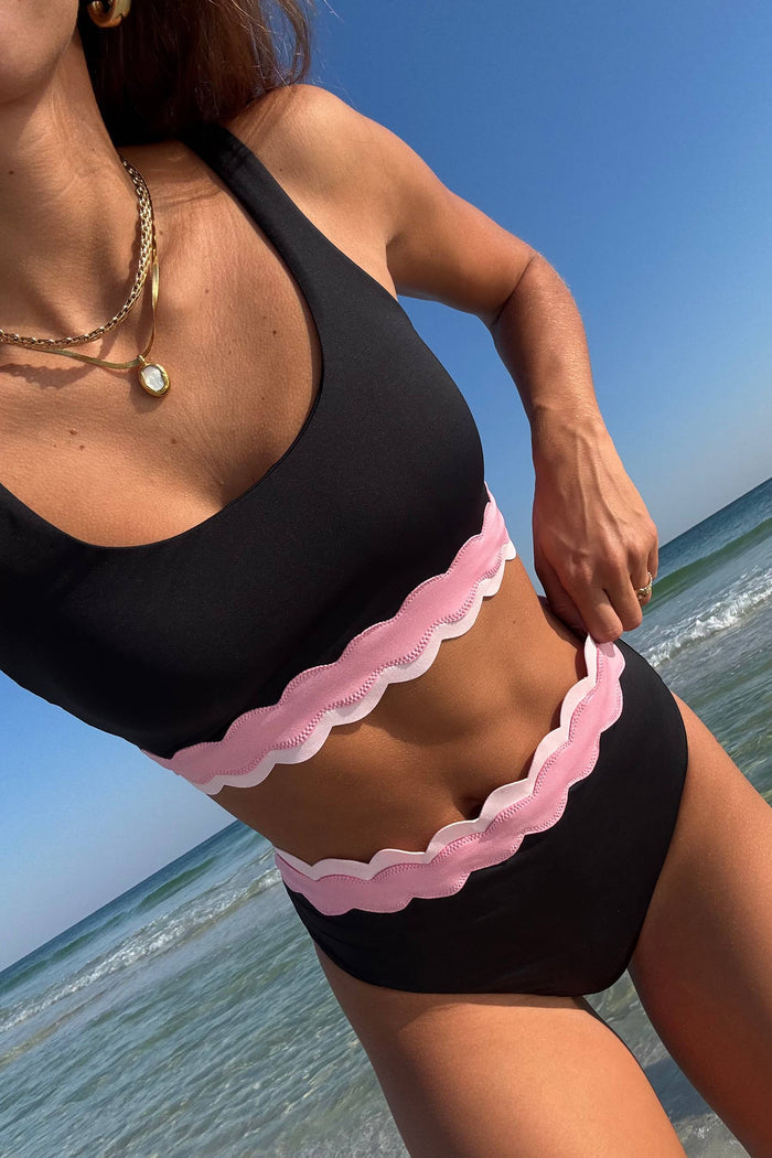 black bralette style swim top with pink contrast wavy trim and a black high waist bottom with pink wavy trim and the top of the waist band