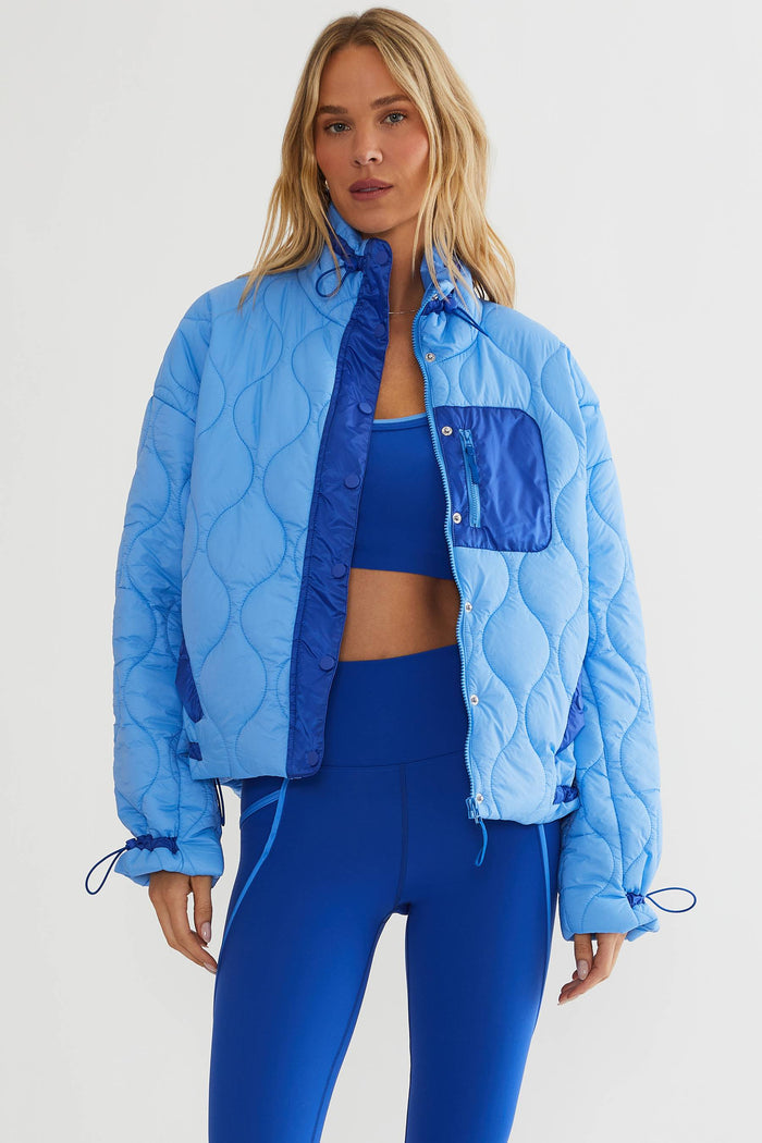 Woman wearing baby blue puffer jacket with royal blue accents.