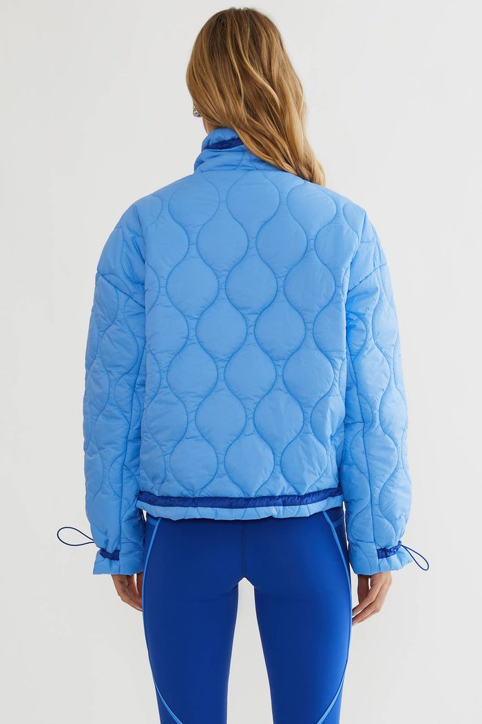 Woman wearing baby blue puffer jacket with royal blue accents.
