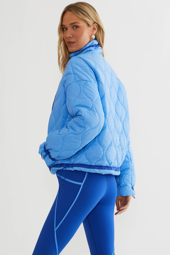 Woman wearing baby blue puffer jacket with royal blue accents.
