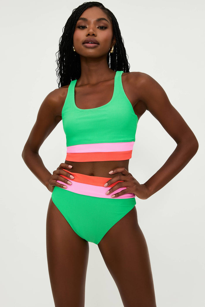 A model is wearing a high-rise green swim bottom with colorblock stripes in pink and white, part of the 'Heidi' collection.