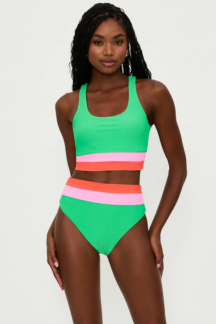 A model is wearing a high-rise green swim bottom with colorblock stripes in pink and white, part of the 'Heidi' collection.