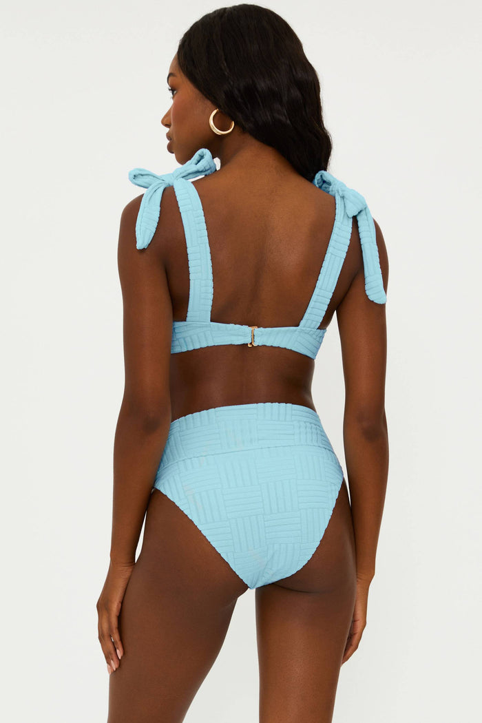 A person wearing a blue high-waisted swim bottom with tie details at the side.