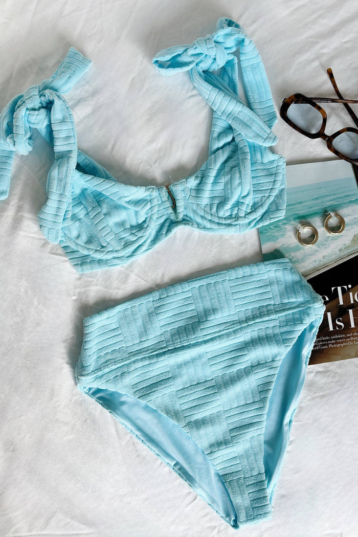A person wearing a blue high-waisted swim bottom with tie details at the side.