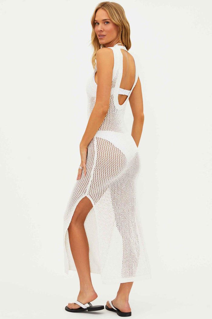 A model wearing a white, open knit, midi length dress with side slits and an open back detail. The dress is sleeveless and appears to be made of cotton and polyester blend.