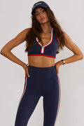 A model wearing a navy blue sports bra with red and white color blocking and a scoop neckline.