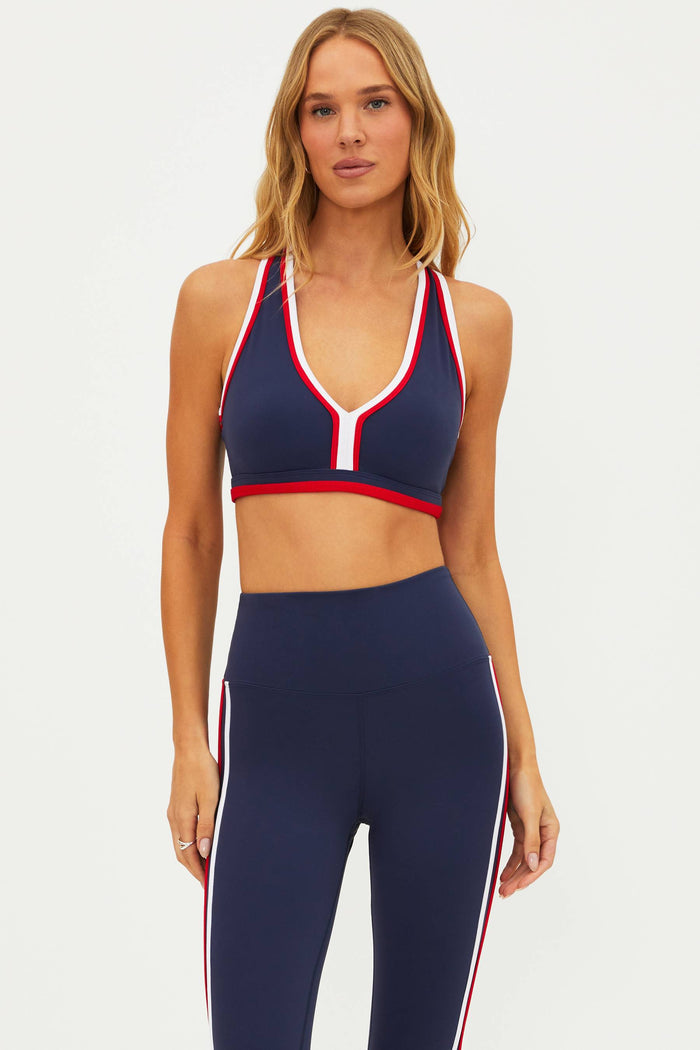 A model wearing a navy and red color-block sports bra with a scoop neckline and racerback design.