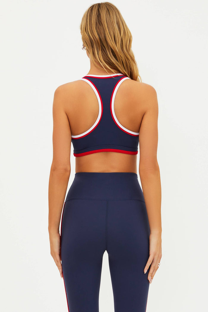 A model wearing a navy blue sports bra with red and white color blocking and a scoop neckline.